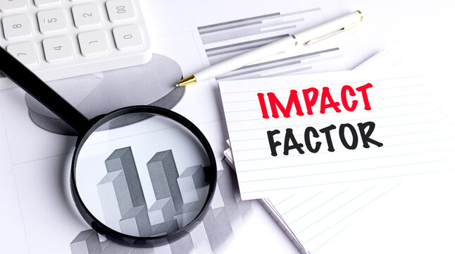 Impact factor phrase on lined paper with magnifying glass, pen, calculator and financial graphs