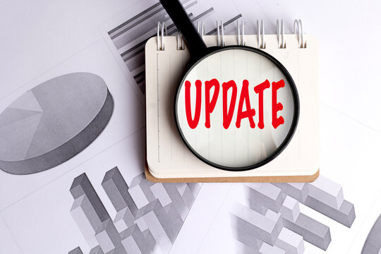 Update word in red letters on notepad under magnifying glass with business graphs in the background