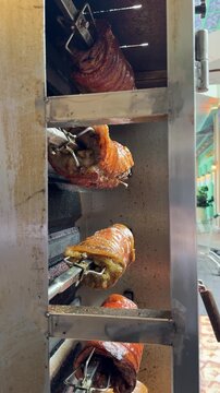 rows of babi guling roasting on metal skewers inside a rotisserie, with golden crispy skin glistening over evenly cooked meat as the pork slowly turns above the heat. the process of roasting porks