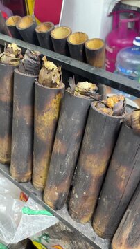 lemang bambu, made from glutinous rice wrapped in banana leaves and cooked inside charred bamboo tubes, slowly roasts over fire. The golden tops show the traditional method of preparing this dish