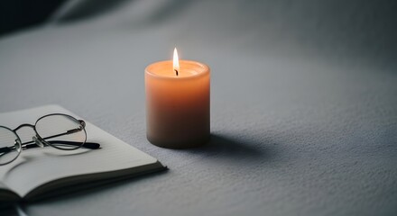 Lit candle beside glasses on an open book on a dark surface with soft shadows.