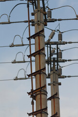Detailed view of electrical power poles with wires and insulators against a cloudy sky, showcasing infrastructure for electricity distribution.