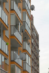 A close-up view of modern residential buildings featuring multiple satellite dishes on balconies, showcasing urban living in a contemporary setting.