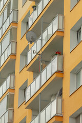 A vibrant yellow apartment building featuring several balconies with modern railings and a satellite dish, showcasing urban living.