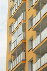A close-up view of a contemporary yellow apartment building showcasing multiple balconies and glass railings, emphasizing modern architecture.