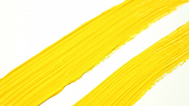 Artist's brush is captured up close as it creates multiple yellow paint strokes in parallel on a blank canvas, resulting in captivating abstract contemporary artwork