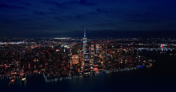 Red light flashes on the steeple of the skyscraper in the downtown of New York. Approaching the waterfront of the city from above the river at night. Aerial view.