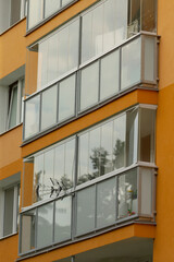 A close-up view of modern balconies featuring glass railings, showcasing the vibrant orange facade of an urban apartment building.