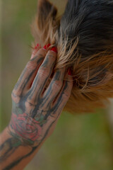 A close-up of a tattooed hand with vivid designs, delicately touching the hair, creating an intimate and artistic moment.