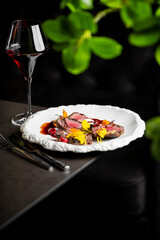 Gourmet sliced sirloin steak with red wine reduction sauce, cranberries, and yellow edible flowers on a white plate in a fine dining restaurant
