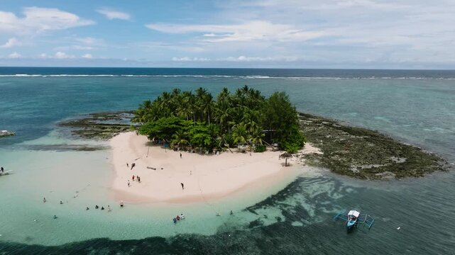 Tourists swimming and relaxing near a small sandy island with palm trees. Guyam Island. Siargao, Philippines.