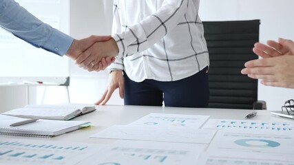 Business partnership success concept with handshake in modern office, financial charts, graphs and laptop on desk representing teamwork, agreement and corporate growth - Powered by Adobe