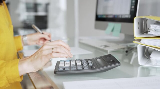 Woman in yellow blouse calculating finances, managing budget, doing taxes, working on accounting documents in office workspace. Audit and taxes in business