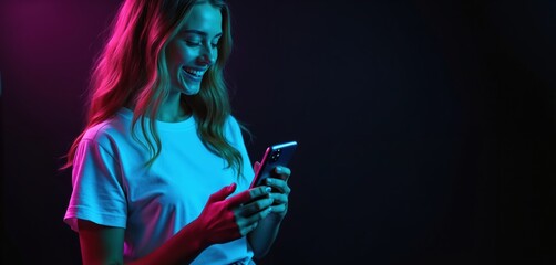 Young woman holds smartphone, smiles, happy. She uses mobile phone in blue, pink neon light on dark backdrop. Girl enjoys social media, digital communication, modern tech, online world.