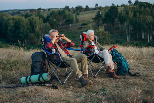 Man with grey beard watches nature through compact binoculars 