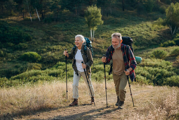 Athletic elderly man and woman hike in hilly autumn countryside
