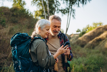 Senior hikers studies smartphone map while walking in natural narrow valley