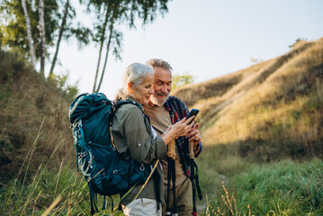 Naklejka premium Senior couple studies smartphone map during hike at hilly countryside 