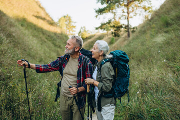 Mature man points route ahead and smiling woman partner nods griping trekking poles