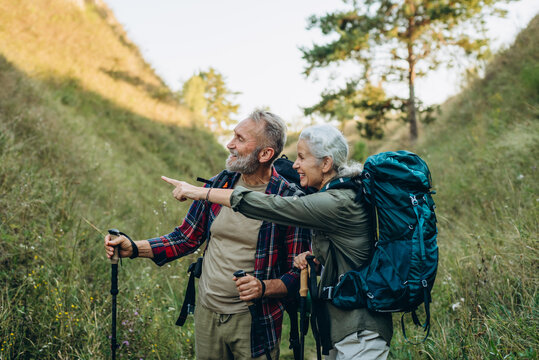 Mature woman points route ahead and smiling senior man partner nods gripping trekking poles
 - Powered by Adobe