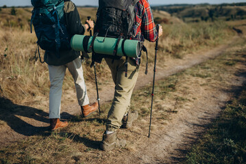 Skilled hikers with walking poles walk along empty country road on autumn day rear view