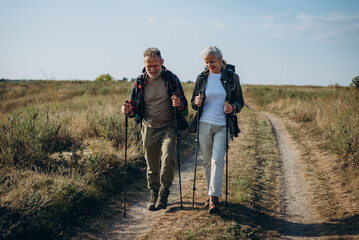 Mature man and woman with backpacks and walking poles hike at fall countryside 
