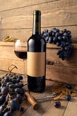 Fototapeta premium Bottle of red wine and blue grapes on a old wooden table.