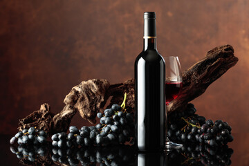 Bottle and glass of red wine with an old snag and blue grapes.