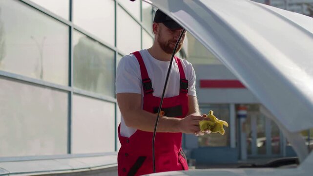 Mechanic in red overalls working on car engine with computer connection, focused on vehicle diagnostics and repair, showcasing modern automotive technology and expertise