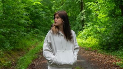 A young woman in a light beige hoodie in the forest looking to the side