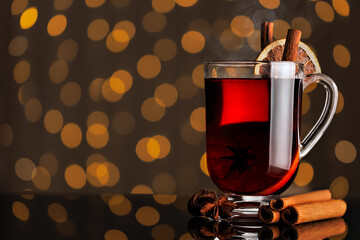 steaming hot mulled wine with cinnamon and anise stars in glass mug on background with bokeh lights