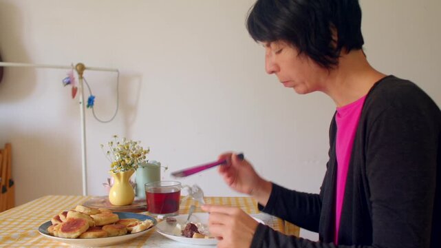 asian woman eating breakfast at simple dining table pancakes tea vase sunlight focused morning ritual slow sip