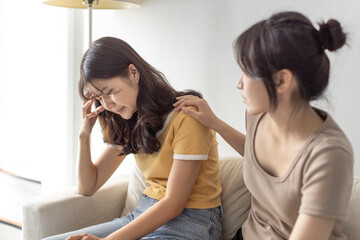 young woman supporting and comforting her sad friend while sitting on the sofa at home.