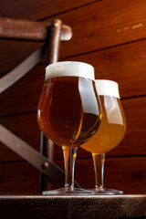 Two elegant glasses of craft beer sit on a dark wooden table, showcasing a rich amber and light golden brew. The warm wood creates a welcoming atmosphere perfect for relaxation