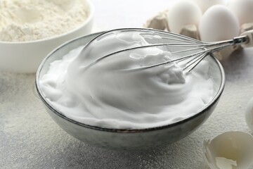 Beating egg whites in bowl, whisk, eggshell and flour on grey textured table, closeup