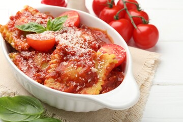 Delicious ravioli with tomato sauce, cheese and basil in baking dish on white wooden table, closeup