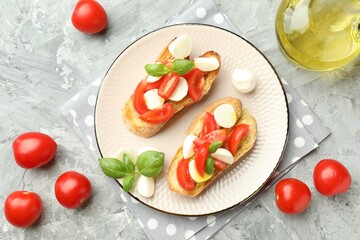 Tasty bruschettas with mozzarella cheese, tomatoes and basil on grey textured table, flat lay