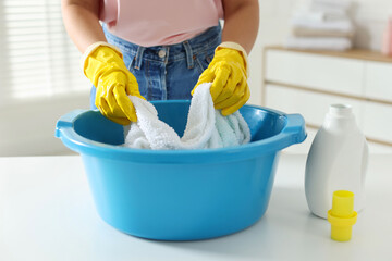 Woman washing towels in plastic basin at white table indoors, closeup