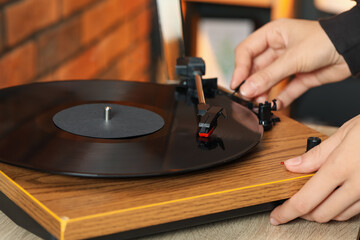Woman turning record player with vinyl disk on at home, closeup