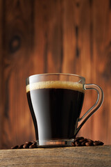 Cup of hot espresso stand on table with coffee beans scattered around it against wooden background
