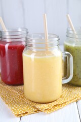 Different tasty smoothies in mason jars on white wooden table