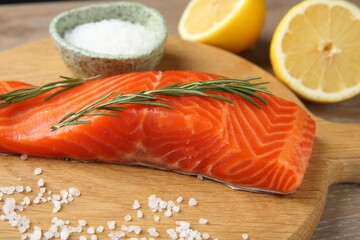 Piece of salmon fillet, rosemary, salt and lemon on wooden table, closeup