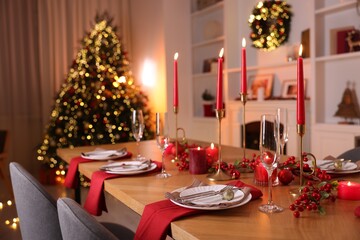 Stylish Christmas table setting with plates, glasses and burning candles in festive decorated room. Bokeh effect