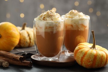 Tasty pumpkin latte with whipped cream, spices and fresh vegetables on black table against blurred lights, closeup