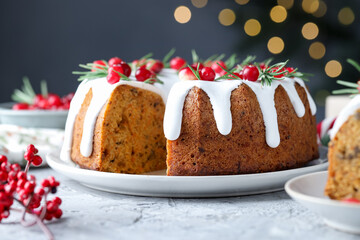 Delicious cut Christmas cake with icing, cranberries and rosemary on grey textured table against blurred lights, closeup. Bokeh effect