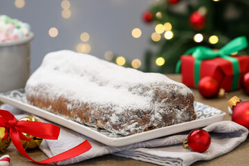 Traditional Christmas Stollen with icing sugar, festive decor and marshmallows on wooden table, closeup. Bokeh effect
