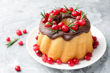 Delicious Christmas cake with chocolate glaze, cranberries and rosemary on light grey textured table, closeup