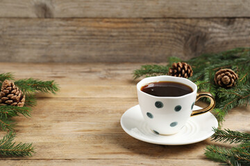 Aromatic coffee in cup, fir tree branches and cones on wooden table, closeup with space for text. Christmas greeting card