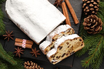 Fototapeta premium Traditional Christmas Stollen with icing sugar, spices and festive decor on black table, flat lay