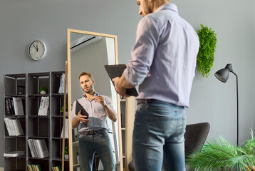Man job seeker rehearses interview speech before office mirror. Holding clipboard, he practices answers and refines gestures for thorough preparation. Confident rehearsal and recruitment.